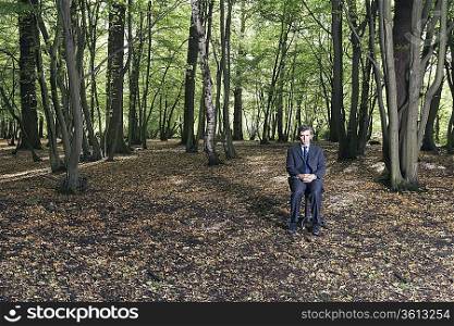 Portrait of business man sitting on office chair in middle of forest