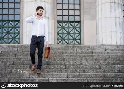 Portrait of business man talking on the phone while standing on stairs outdoors. Business and success concept. 