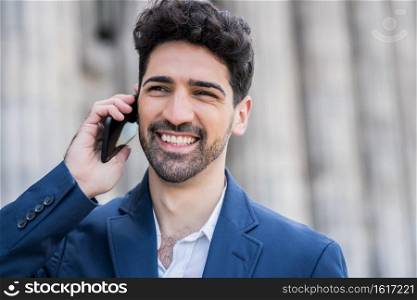 Portrait of business man talking on the phone while standing outdoors on the street. Business and success concept. 