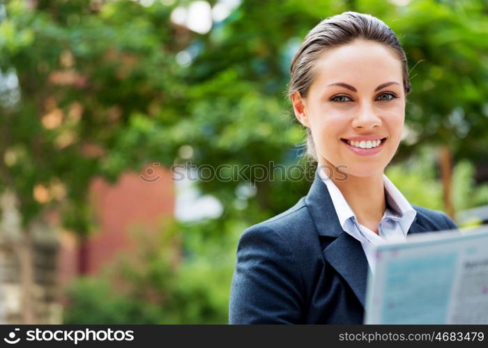 Portrait of business woman smiling outdoor. Portrait of young business woman reading newspaper outdoors