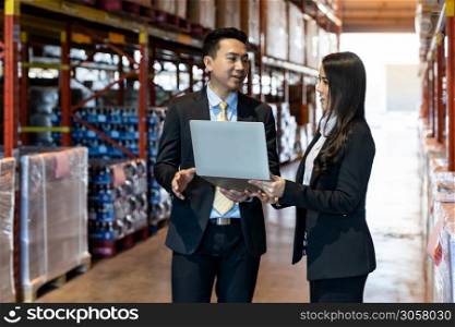Portrait of businessman discuss with businesswoman wit computer laptop about inventory with factory large distribution warehouse. Business investment merger acquisitions concept.