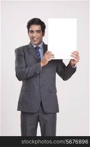 Portrait of businessman holding empty placard over gray background