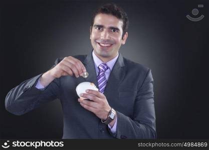 Portrait of businessman putting coin in piggy bank