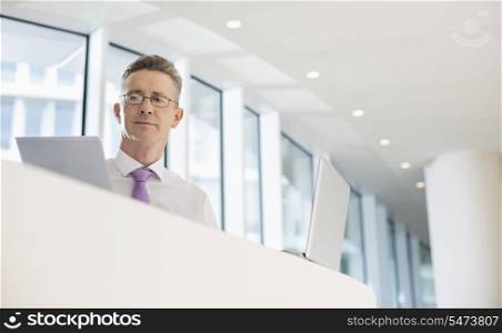 Portrait of businessman with laptop and documents at railing