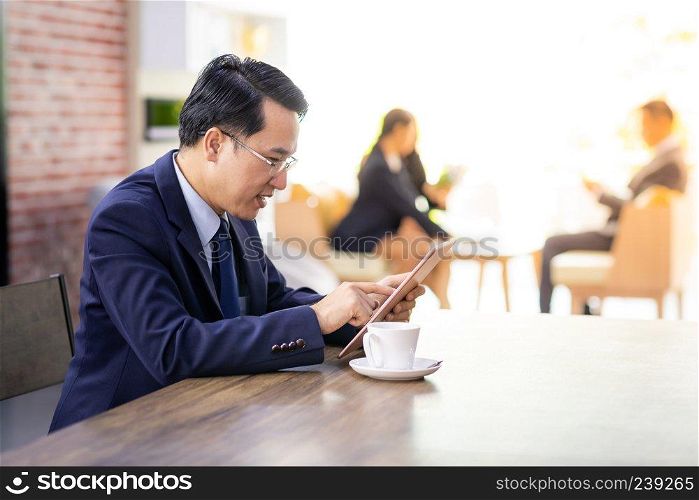 Portrait of Businessman working in cafe with smart phone and tablet with business team in background using for coporate background work