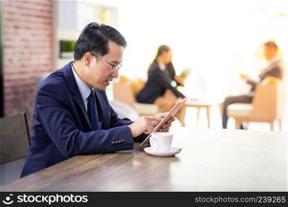 Portrait of Businessman working in cafe with smart phone and tablet with business team in background using for coporate background work