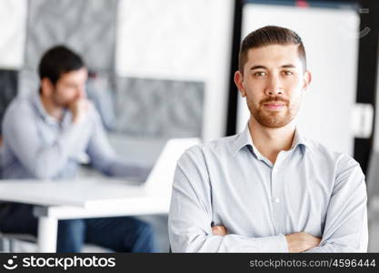 Portrait of businessman. Young businessman standing in offfice with arms crossed