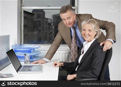 Portrait of businesswoman and man with laptop at desk in office