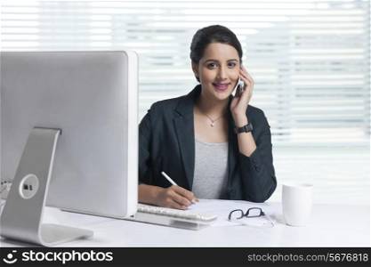 Portrait of businesswoman answering mobile phone while working at office desk
