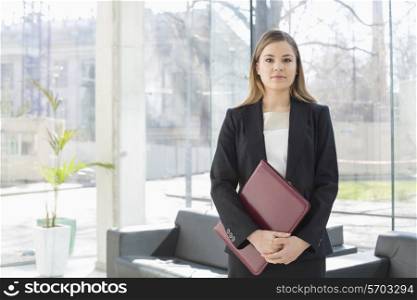 Portrait of businesswoman holding file while standing at office lobby
