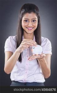 Portrait of businesswoman putting coin in piggy bank