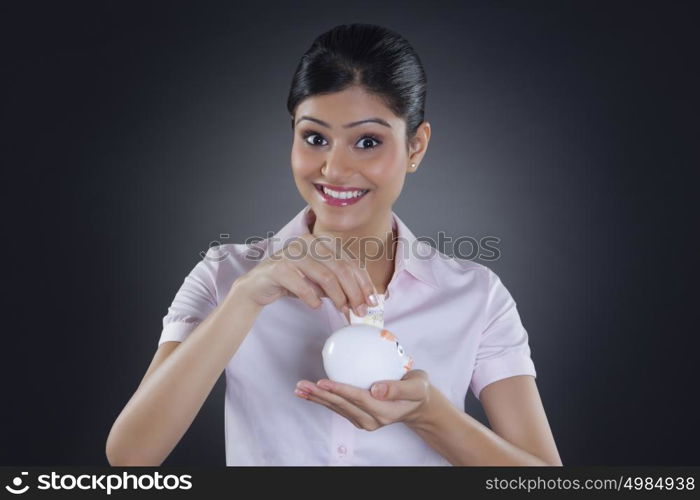 Portrait of businesswoman putting money in piggy bank