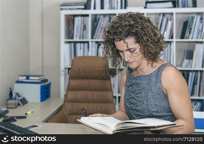 Portrait of businesswoman review notebook in her office against of bookcase. Businesswoman review notebook in office against of bookcase