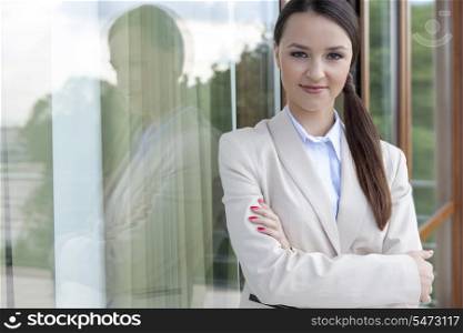 Portrait of businesswoman standing arms crossed by glass door