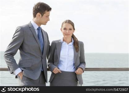 Portrait of businesswoman with coworker leaning on terrace railing against sky
