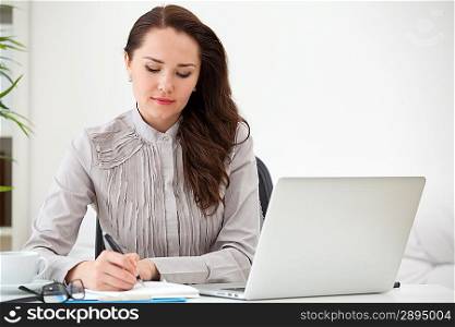 Portrait of businesswoman with laptop writes on a document at office