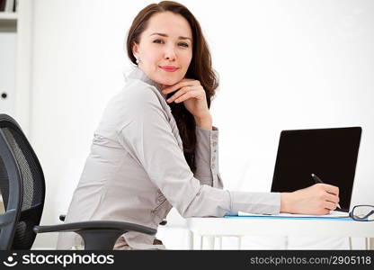 Portrait of businesswoman with laptop writes on a document at office