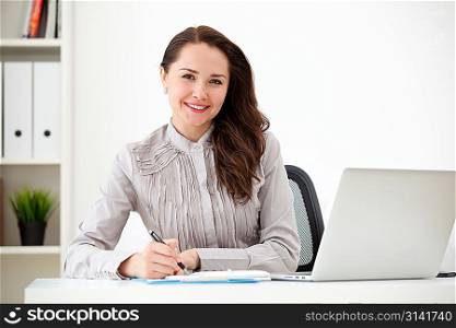 Portrait of businesswoman with laptop writes on a document at office