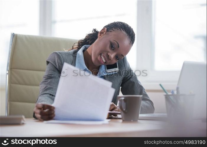 Portrait of businesswoman working with laptop writes on a document and calling phone at her office