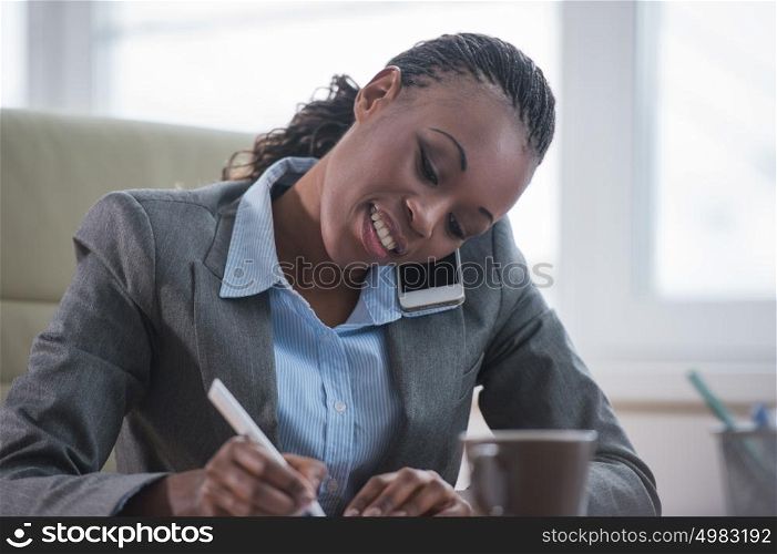 Portrait of businesswoman working with laptop writes on a document and calling phone at her office