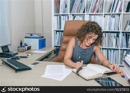 Portrait of businesswoman writing plans in notebook at workplace. Businesswoman writing in notebook sitting in the office