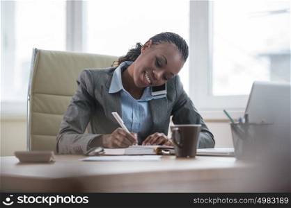 Portrait of busy business woman or secretary writing and typing in working environment