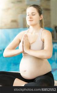 Portrait of calm pregnant woman meditating at swimming pool