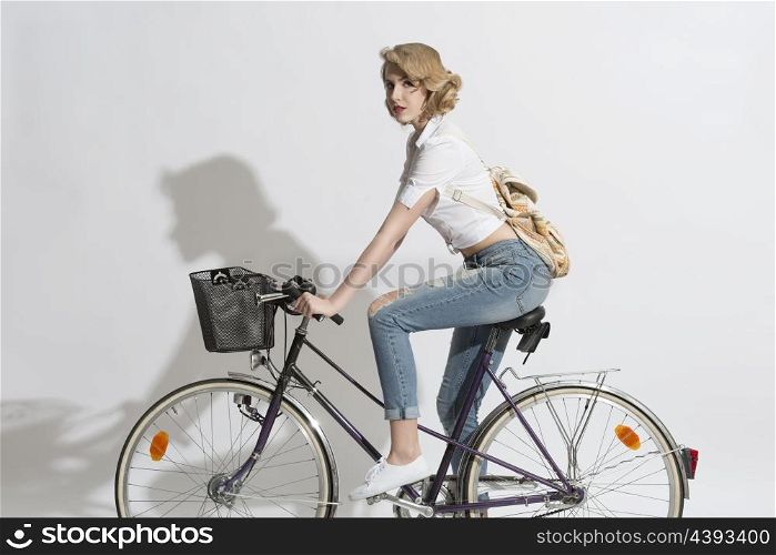 portrait of casual blonde woman with jeans, white shirt and small backpack on a bicycle