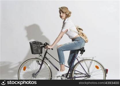 portrait of casual blonde woman with jeans, white shirt and small backpack on a bicycle