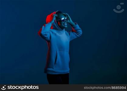 Portrait of casual hipster woman in sunglasses and sweater hood over dark studio background in blue neon light. Casual hipster woman in sunglasses over dark studio wall