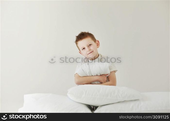 Portrait of casually dressed little boy is hugging white pillow, feeling tired after long full day, with cheerful smile, having rest.. Portrait of casually dressed little boy is hugging white pillow, feeling tired after long full day, with cheerful smile, having rest