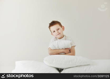 Portrait of casually dressed little boy is hugging white pillow, feeling tired after long full day, with cheerful smile, having rest.. Portrait of casually dressed little boy is hugging white pillow, feeling tired after long full day, with cheerful smile, having rest