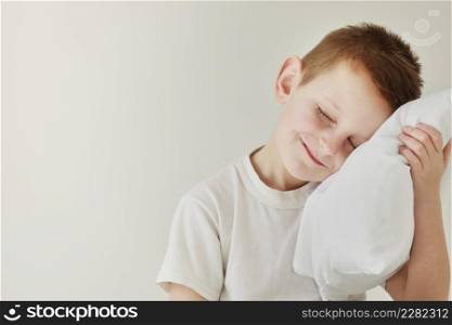 Portrait of casually dressed little boy leaning on white pillow, while hugging it, feeling tired after long full day, with cheerful smile, having rest.. Portrait of casually dressed little boy leaning on white pillow, while hugging it, feeling tired after long full day, with cheerful smile, having rest