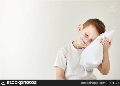 Portrait of casually dressed little boy leaning on white pillow, while hugging it, feeling tired after long full day, with cheerful smile, having rest.. Portrait of casually dressed little boy leaning on white pillow, while hugging it, feeling tired after long full day, with cheerful smile, having rest