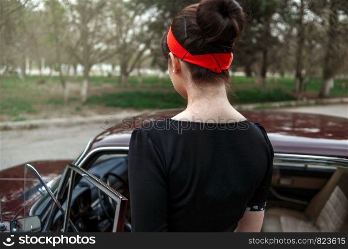 portrait of Caucasian beautiful young girl in black vintage dress who sits in a retro car