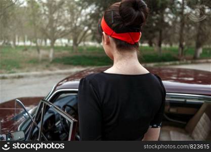 portrait of Caucasian beautiful young girl in black vintage dress who sits in a retro car