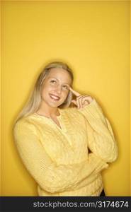 Portrait of Caucasian blond teen girl pointing at her head standing against yellow background.