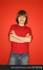 Portrait of Caucasian boy in studio standing against red background with arms crossed.