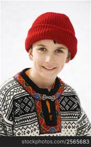 Portrait of Caucasian boy wearing sweater and red winter cap smiling at viewer.