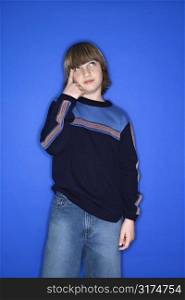 Portrait of Caucasian boy with one hand pointing at his head standing against blue background.