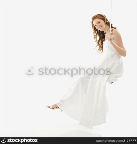 Portrait of Caucasian bride swinging on swing set.
