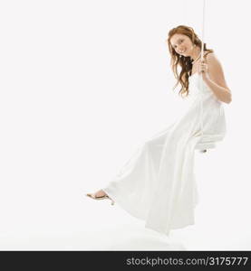 Portrait of Caucasian bride swinging on swing set.