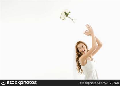 Portrait of Caucasian bride tossing bouquet behind her.