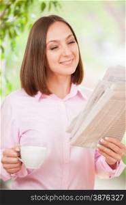 Portrait of caucasian businesswoman reading the newspaper while standing and having a cup of coffee