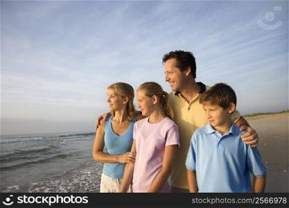 Portrait of Caucasian family of four posing on beach looking at ocean.