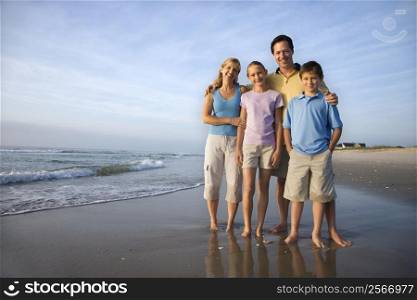 Portrait of Caucasian family of four posing on beach looking at viewer smiling.
