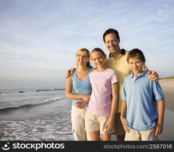 Portrait of Caucasian family of four posing on beach looking at viewer smiling.