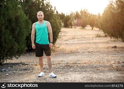 portrait of Caucasian guy in an azure t-shirt and black shorts,who stands on a rough terrain before Jogging