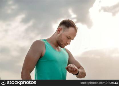 portrait of Caucasian guy in azure t-shirt looking at fitness tracker readings after or before Jogging.