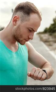 portrait of Caucasian guy in azure t-shirt looking at fitness tracker readings after or before Jogging.